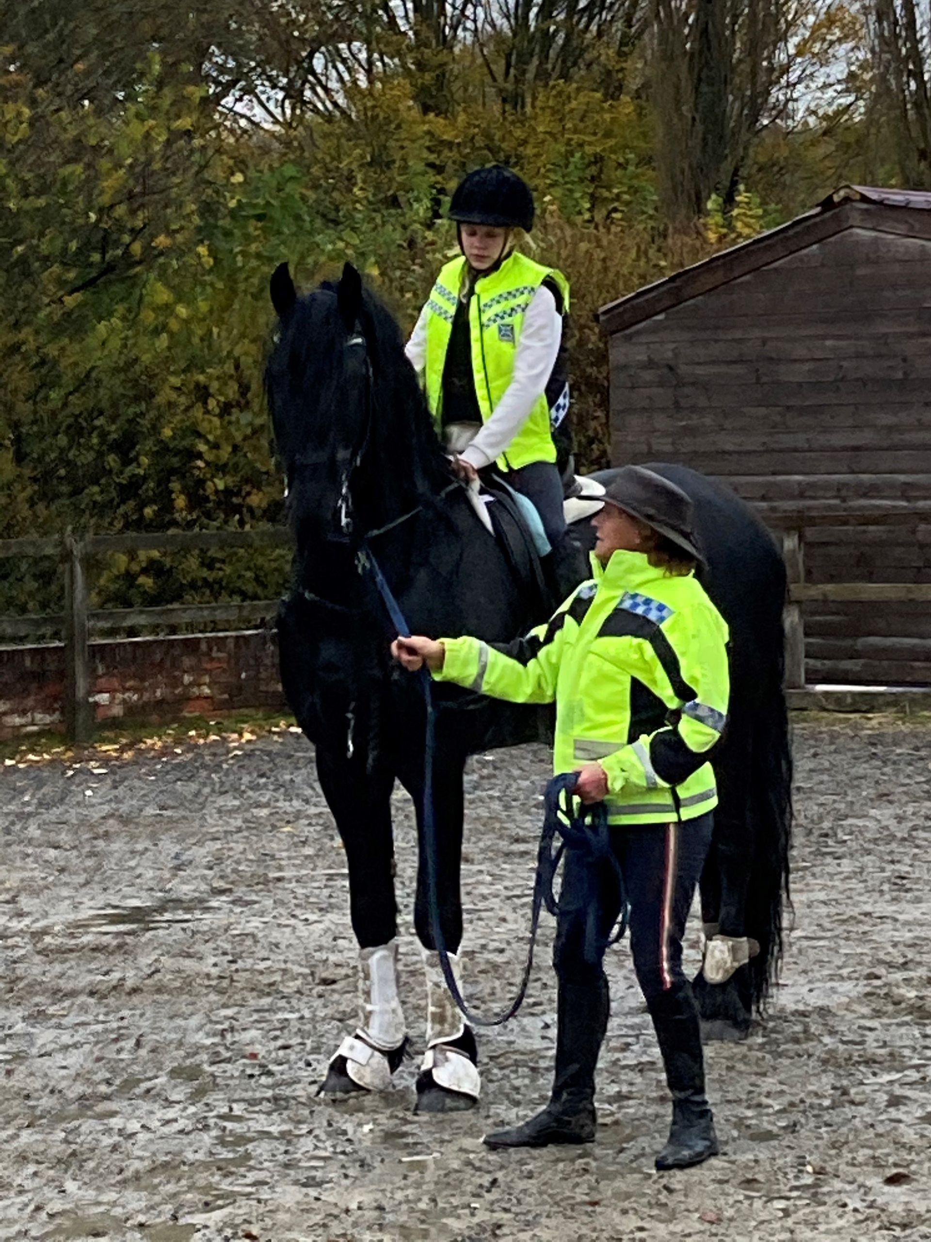 A man and a woman are riding a black horse in a dirt field.