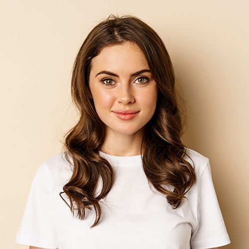 A woman with long brown hair is wearing a white t-shirt and smiling.