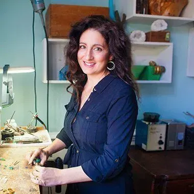 A woman is sitting at a table in a workshop making jewelry.