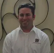 A man in a white shirt is smiling in front of a wall.