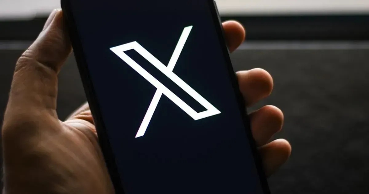 A person is holding a cell phone with the letter x on the screen.