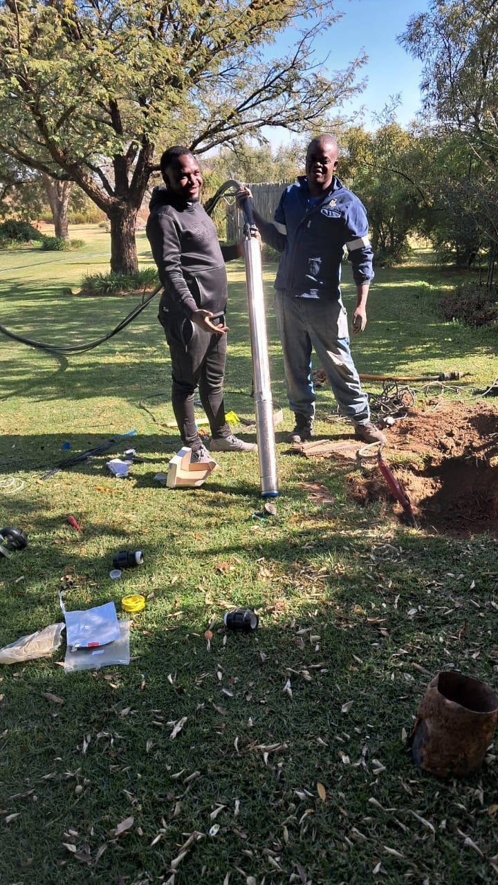 Two men are working on a well in a field.