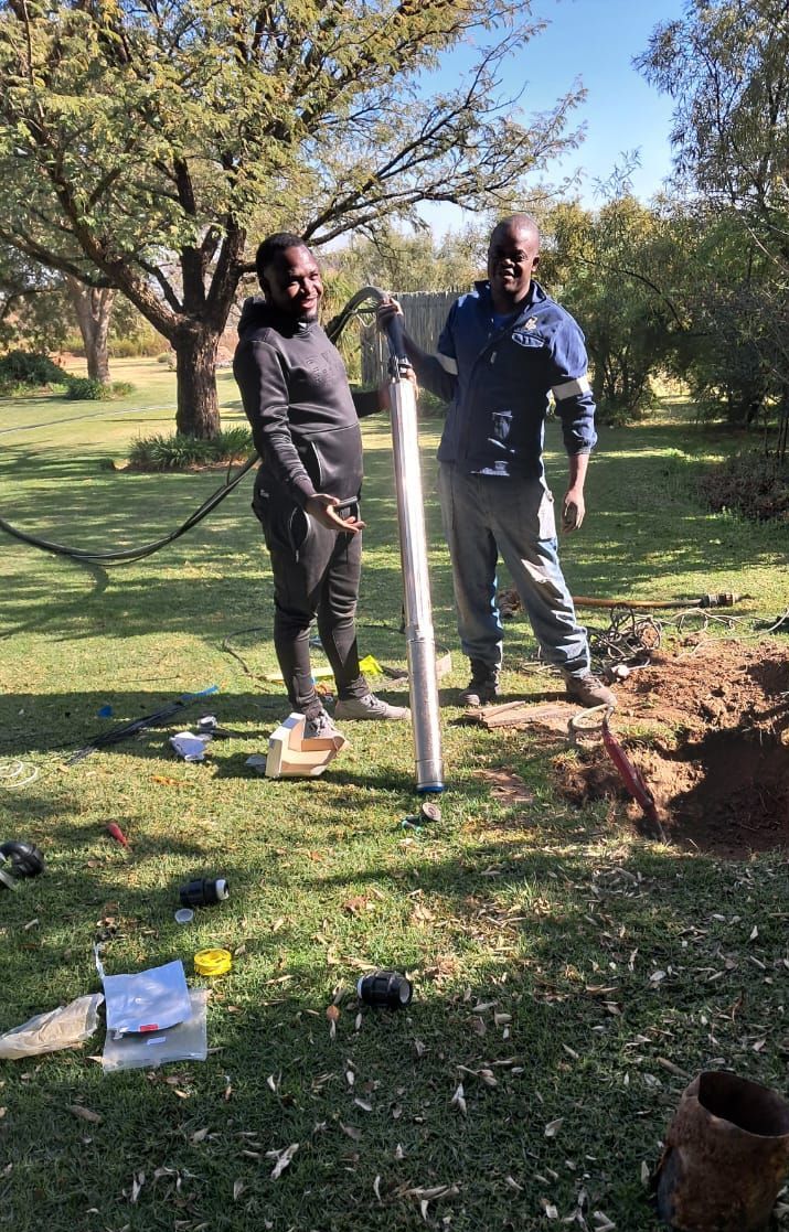 Two men are working on a well in a field.