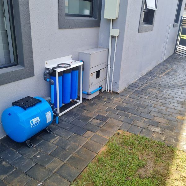 A blue water tank is sitting on the sidewalk next to a building.