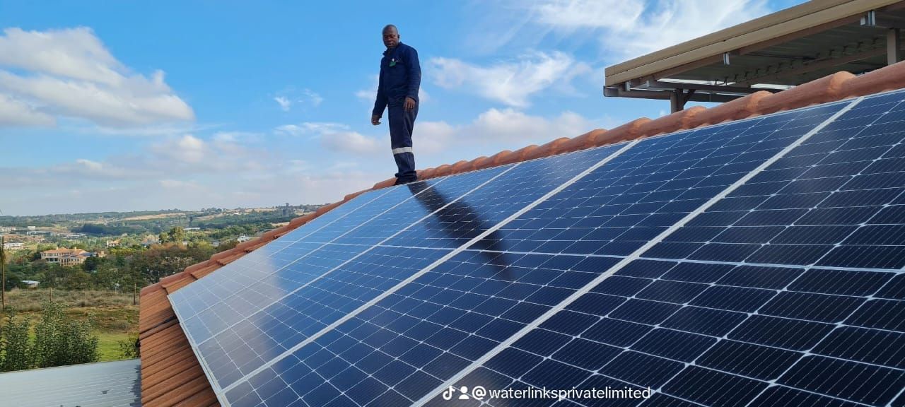 A man is standing on top of a roof with solar panels.