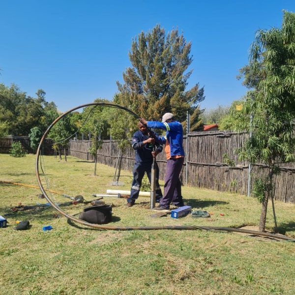 Two men are working on a pipe in a grassy field.