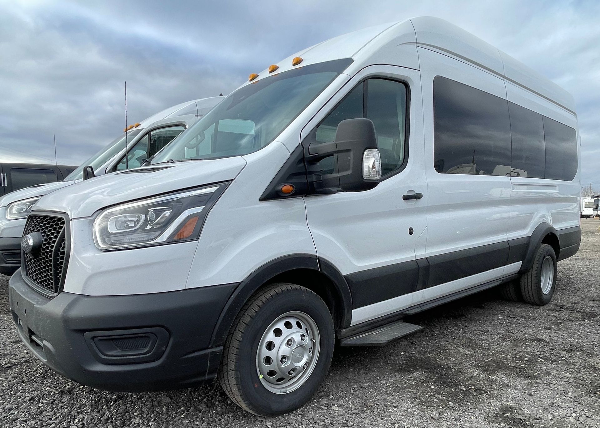 a white Ford Transit executive 13 passenger shuttle van is parked in a gravel lot