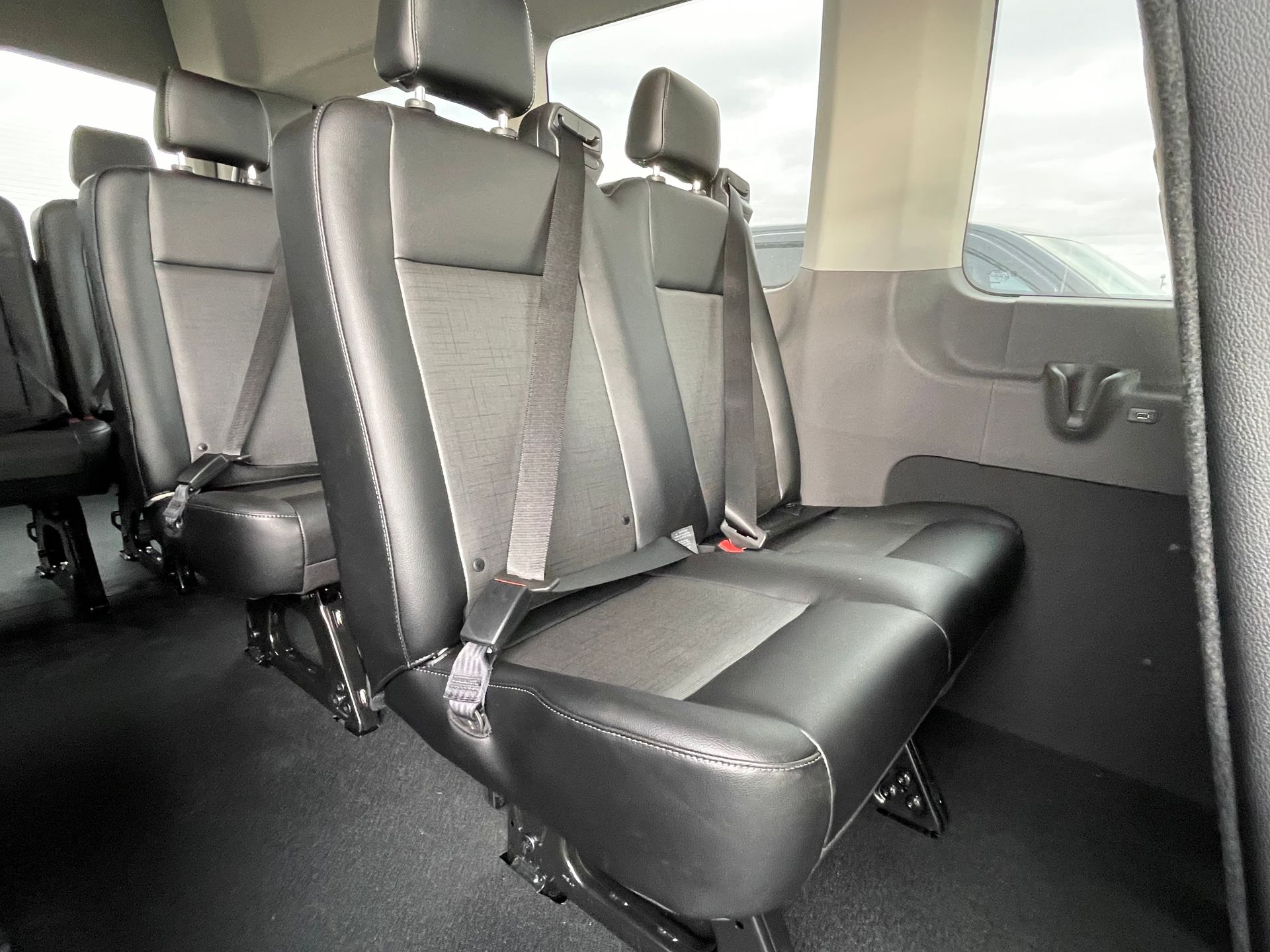 a row of black seats in an executive shuttle van with seat belts