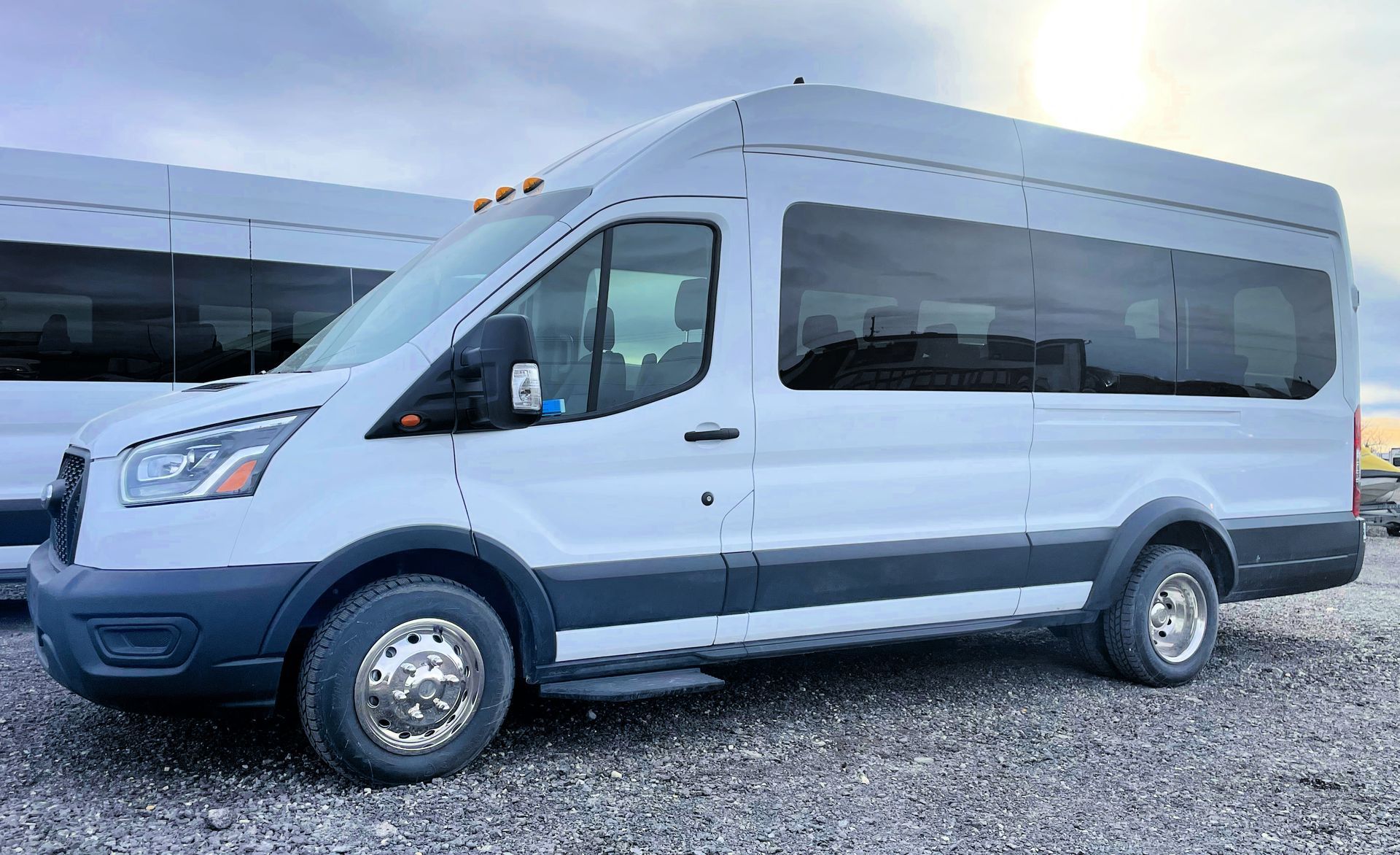 a white Ford Transit executive 13 passenger shuttle van is parked in a gravel lot