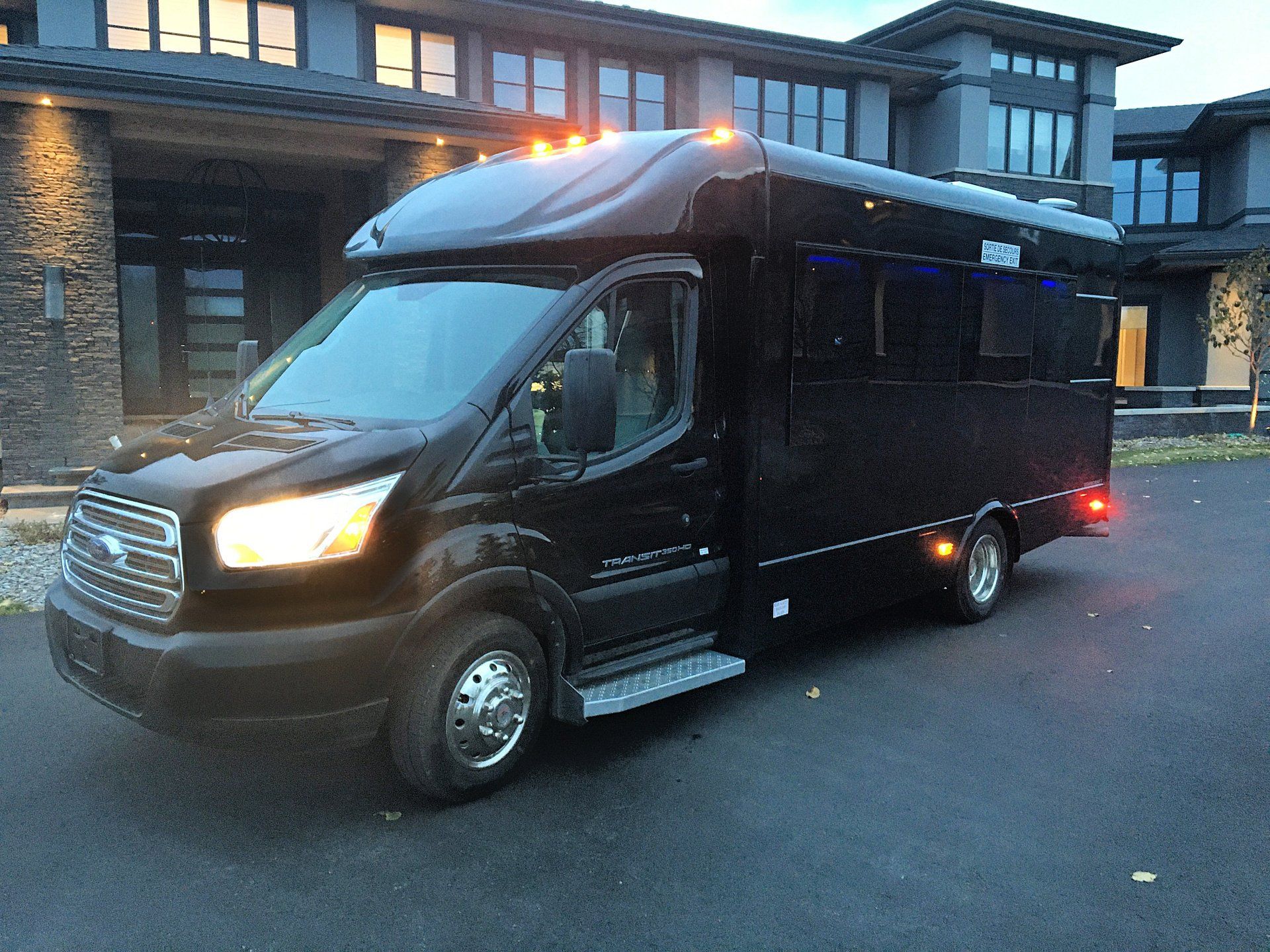a black Battisti Ford Transit Party Bus is parked in front of a large house