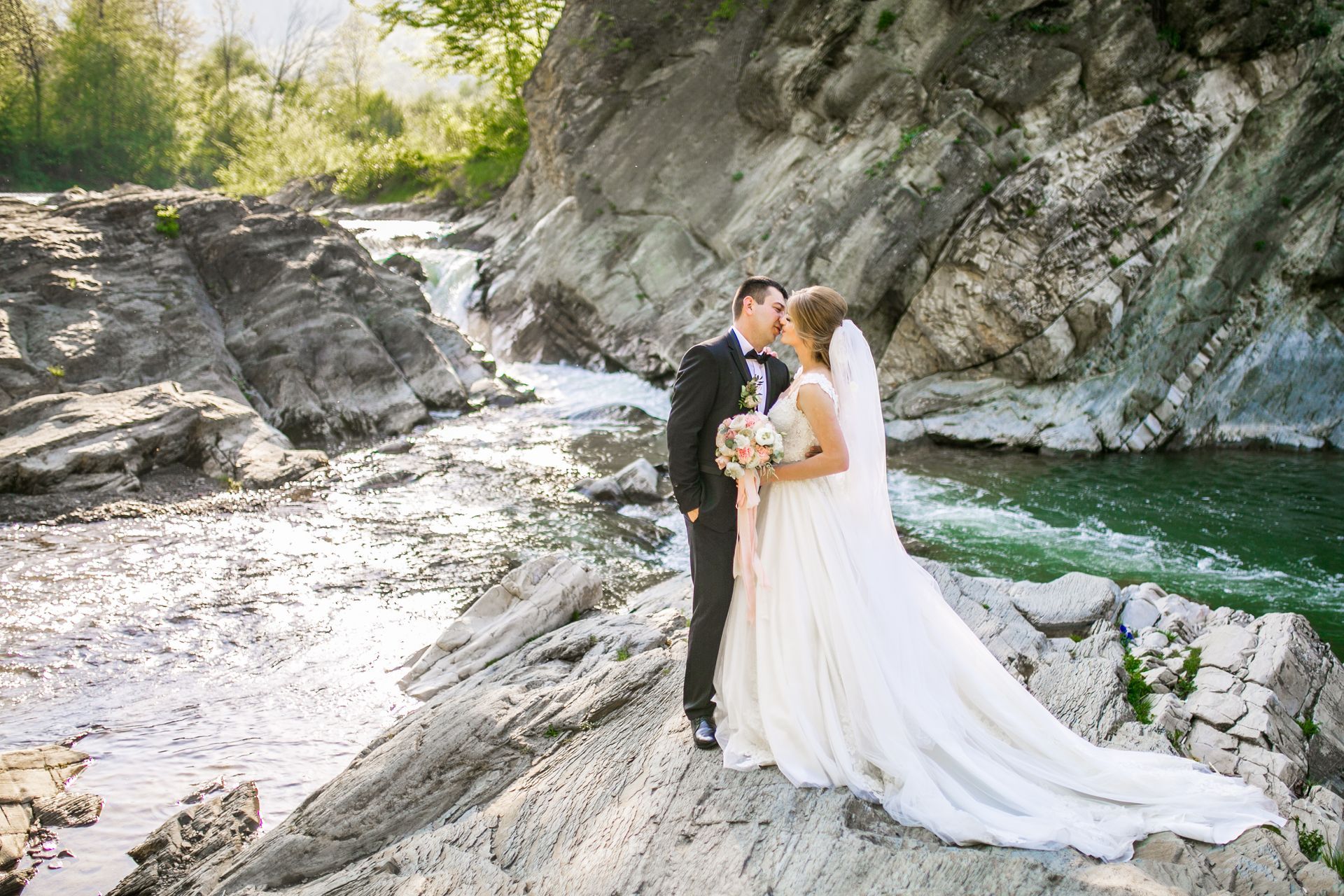 A bride and groom are kissing in front of a river.