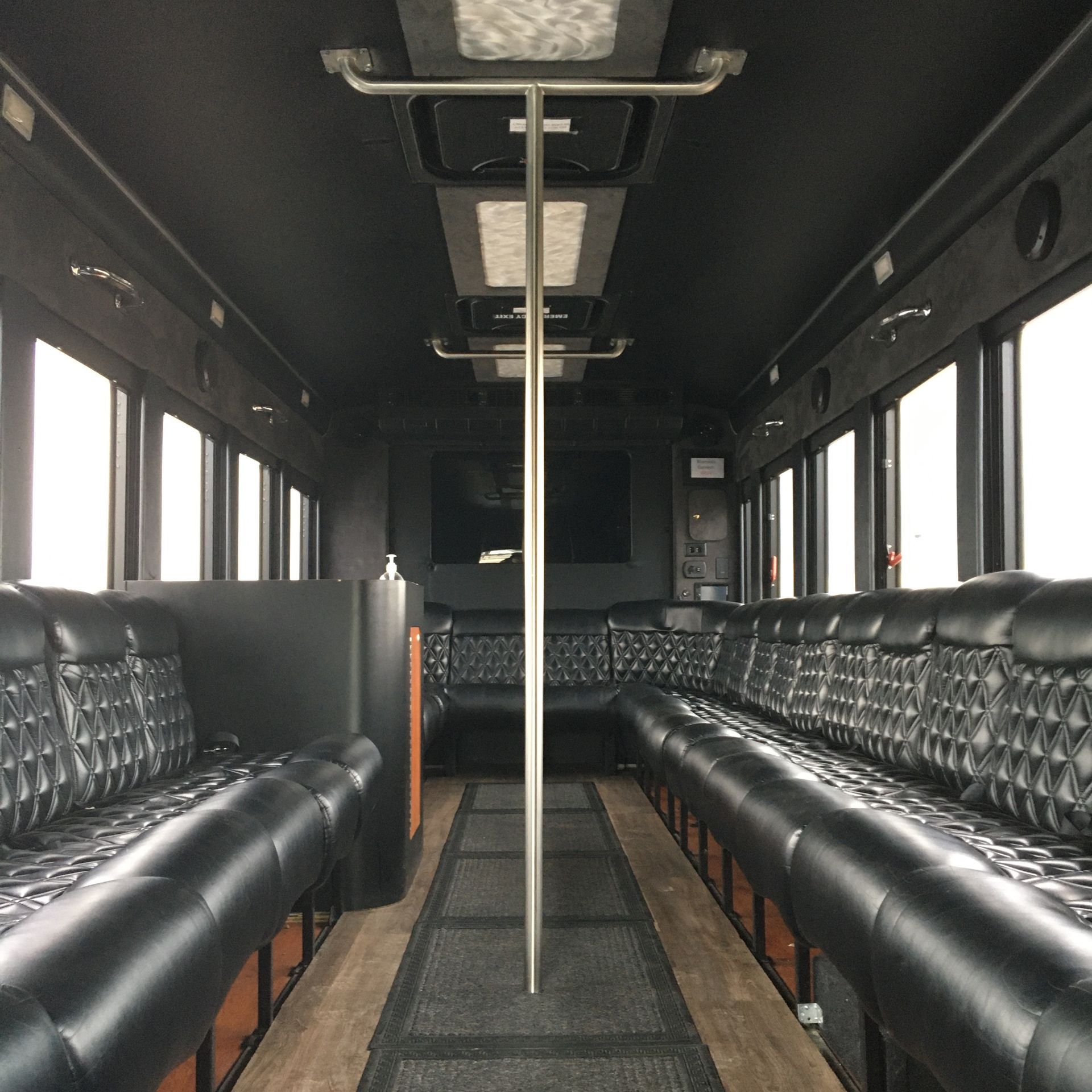 Interior of a black party bus with leather seating, a pole, and overhead lighting.