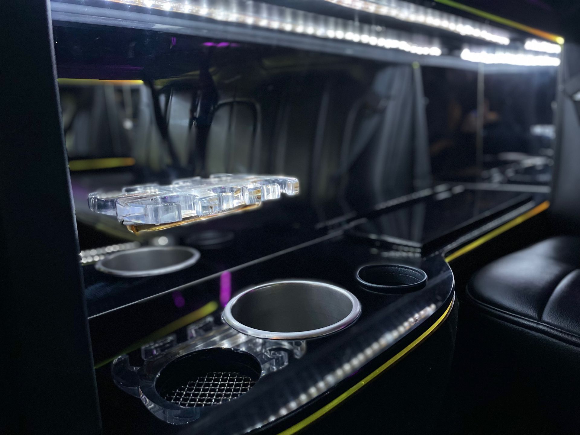 Interior view of a limousine bar area with cup holders, lighting, and glasses.