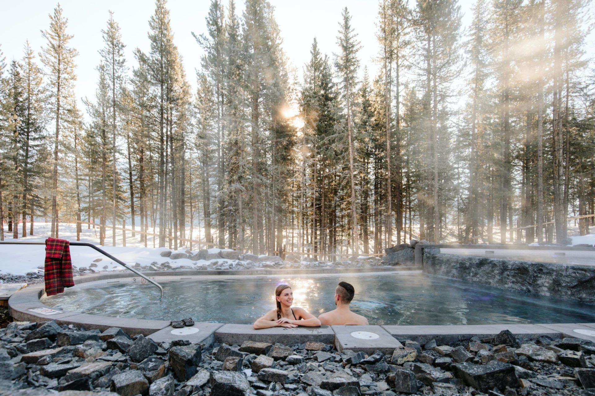 a man and a woman are sitting in a hot tub in the woods .