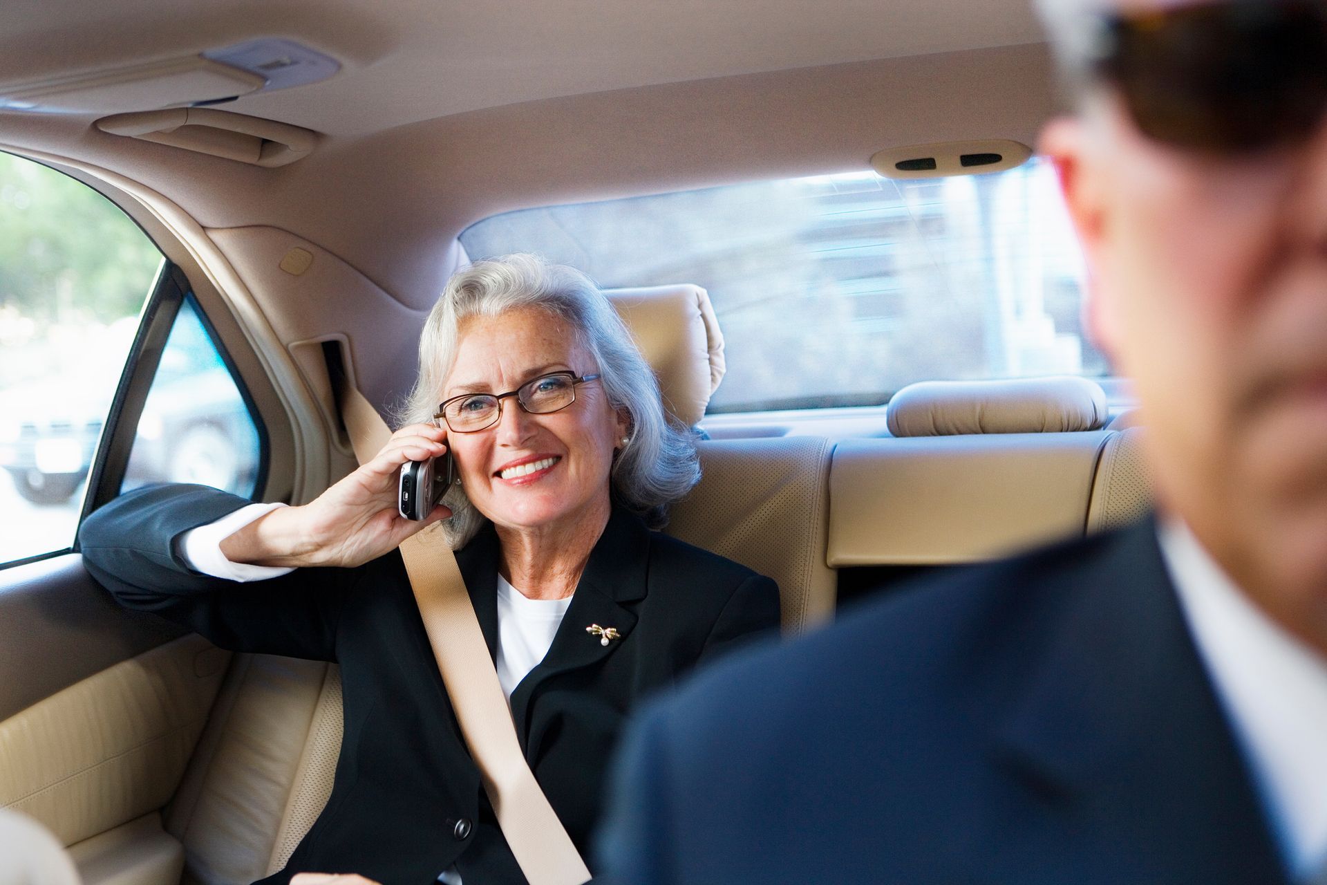 A woman is sitting in the back seat of a car talking on a cell phone.