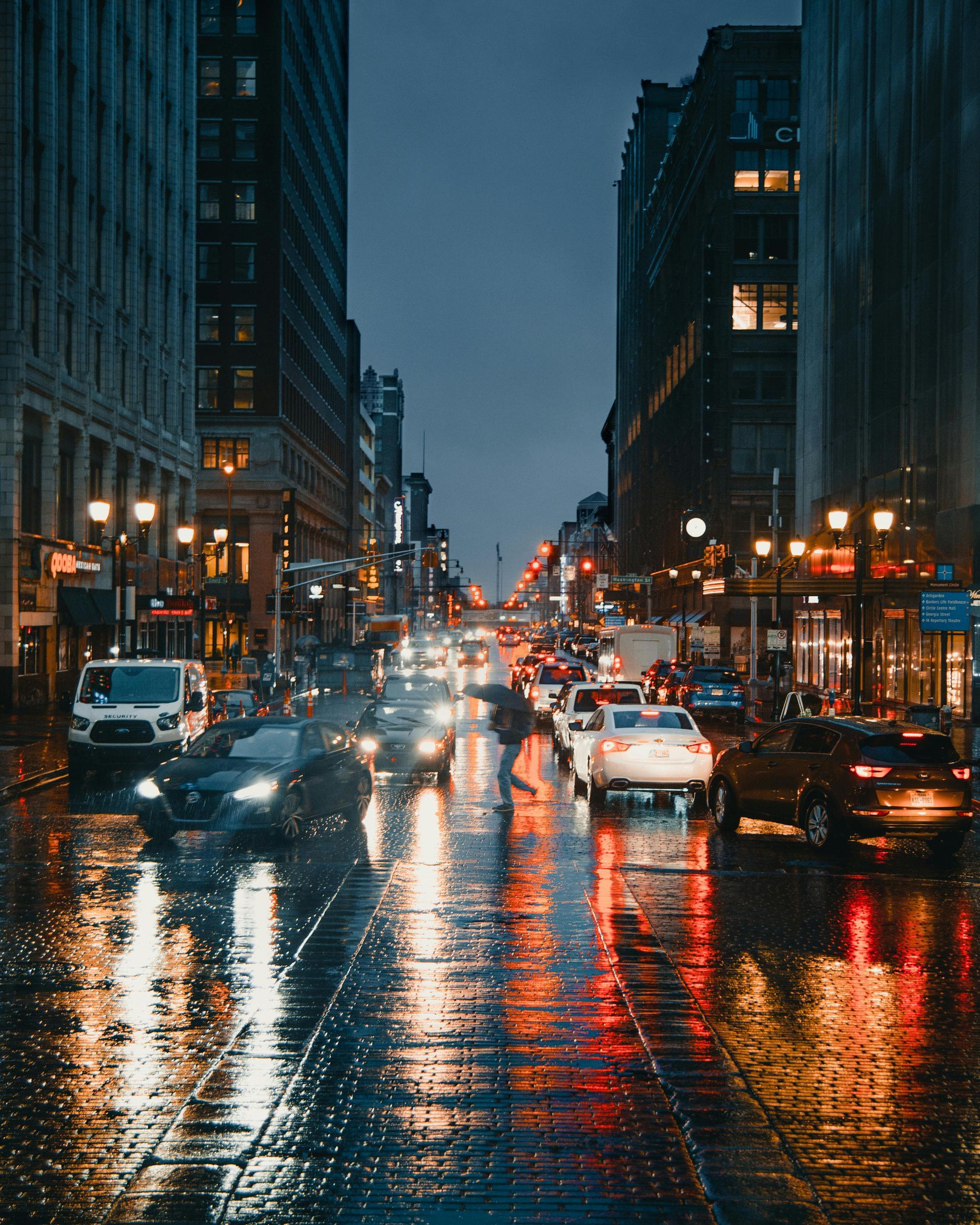 A busy city street in the rain at night with cars driving down it.