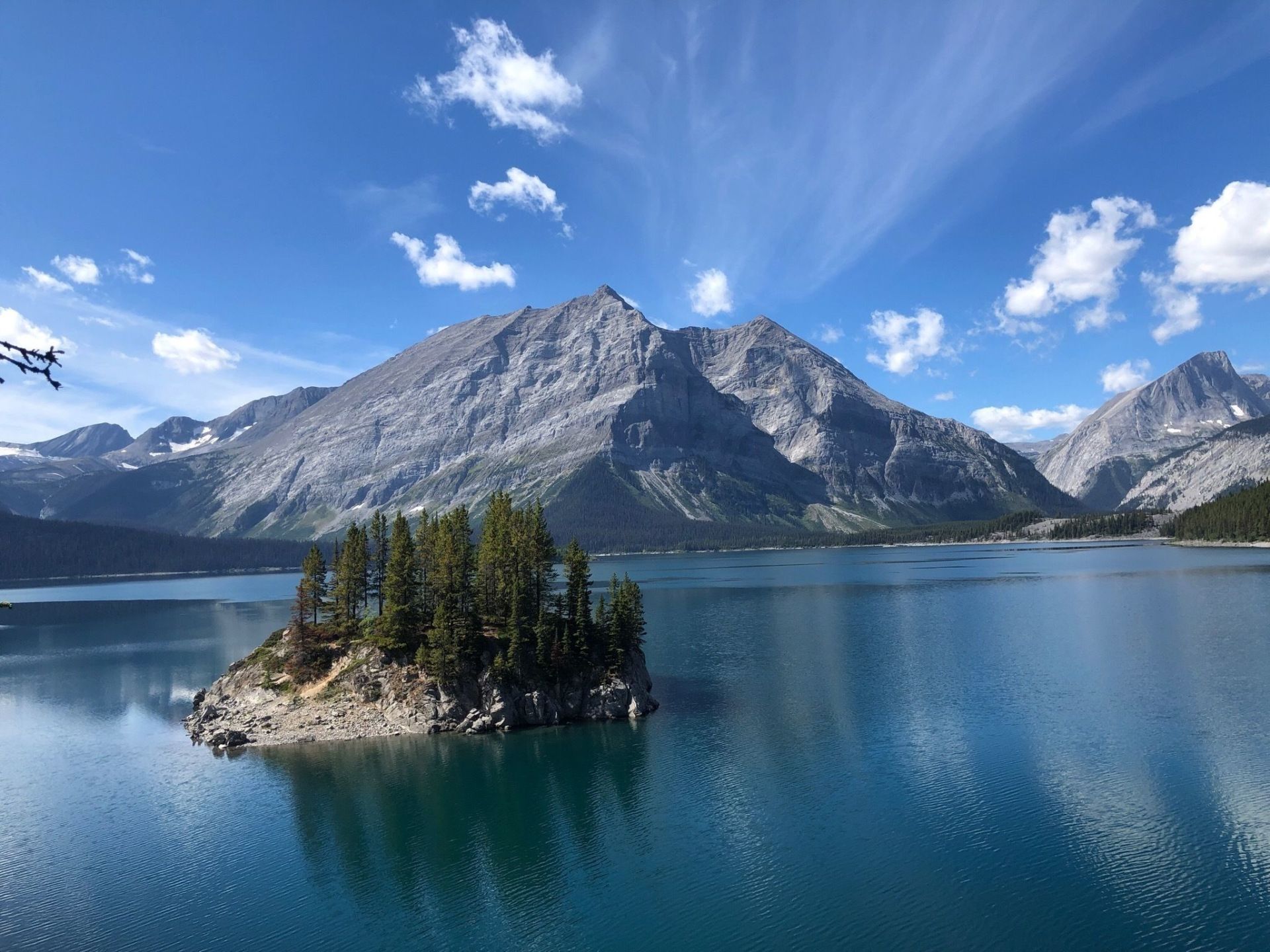 A small island in the middle of a lake with mountains in the background