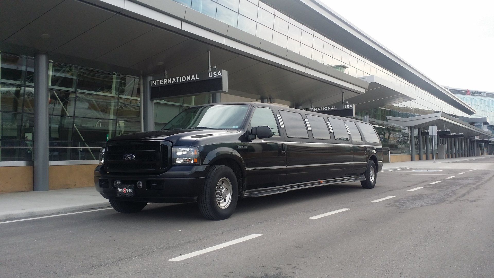 black 14 passenger Excursion limousine parked at Calgary airport International and USA arrivals door