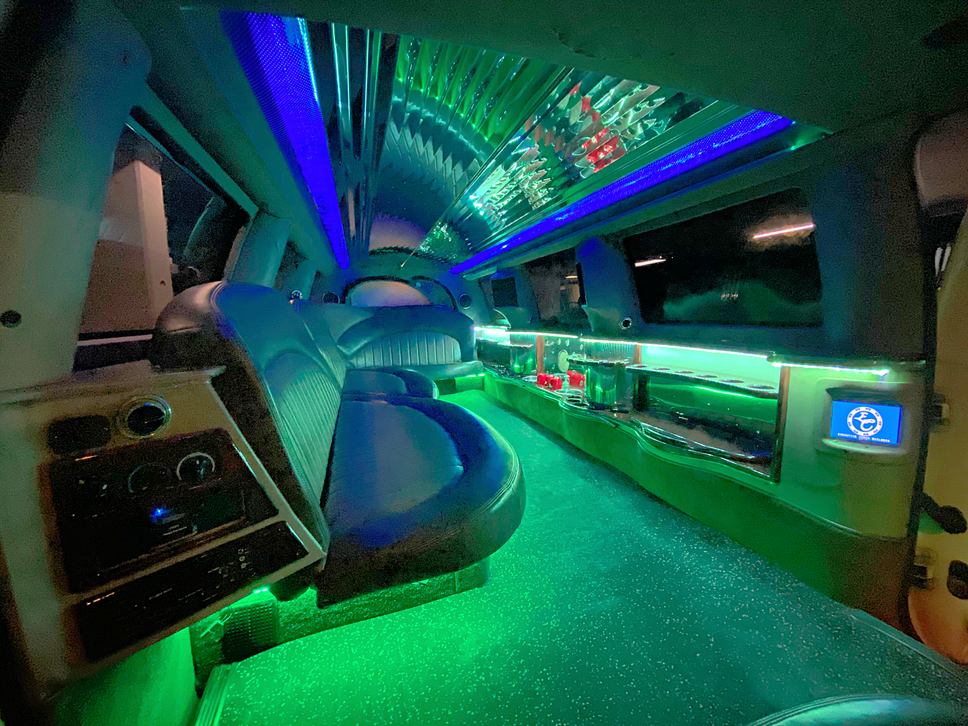 white 14 passenger Excursion limousine interior with green LED back lighting, J seating and full bar area