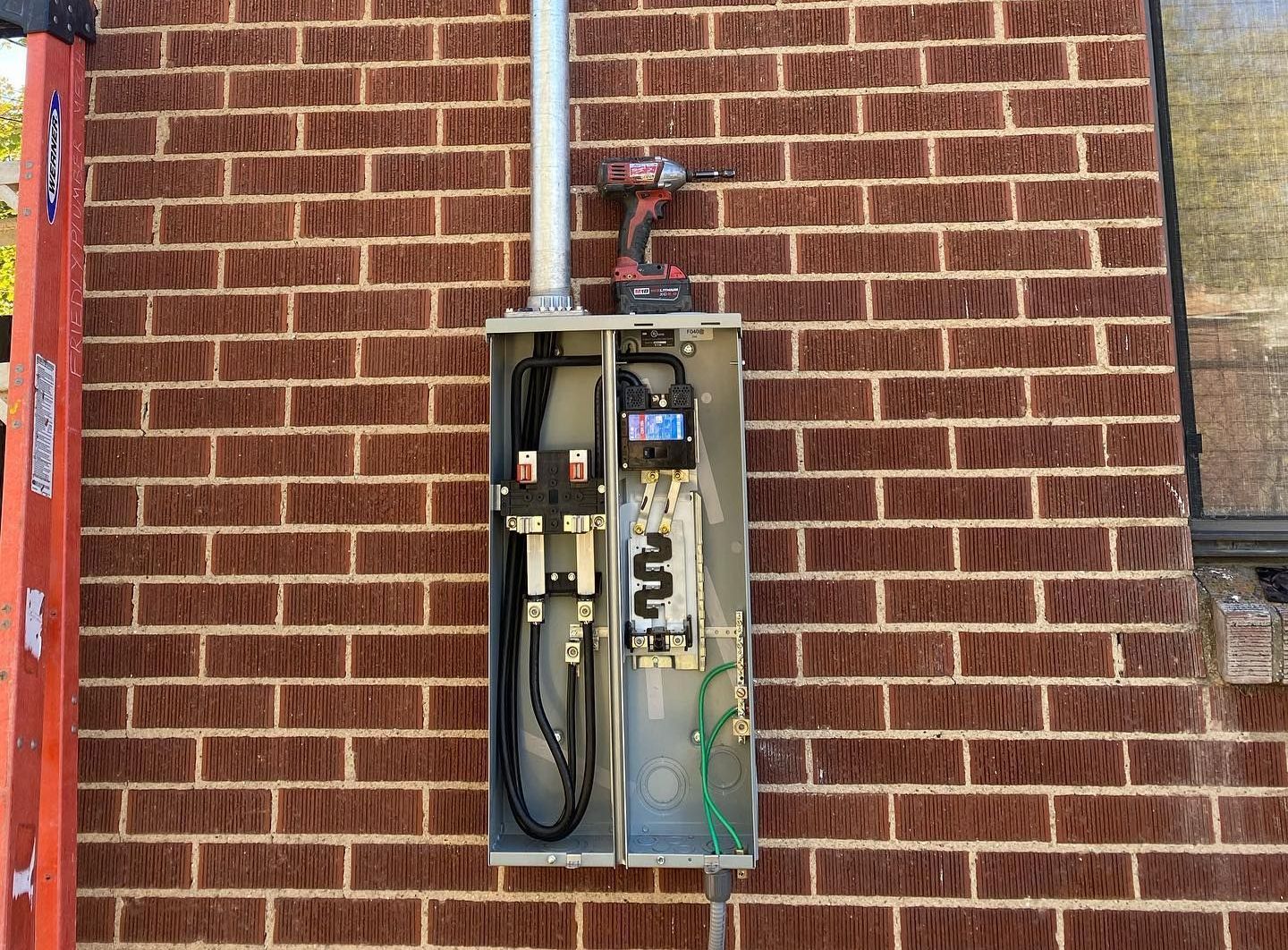 A brick wall with a electrical box and a drill on it.
