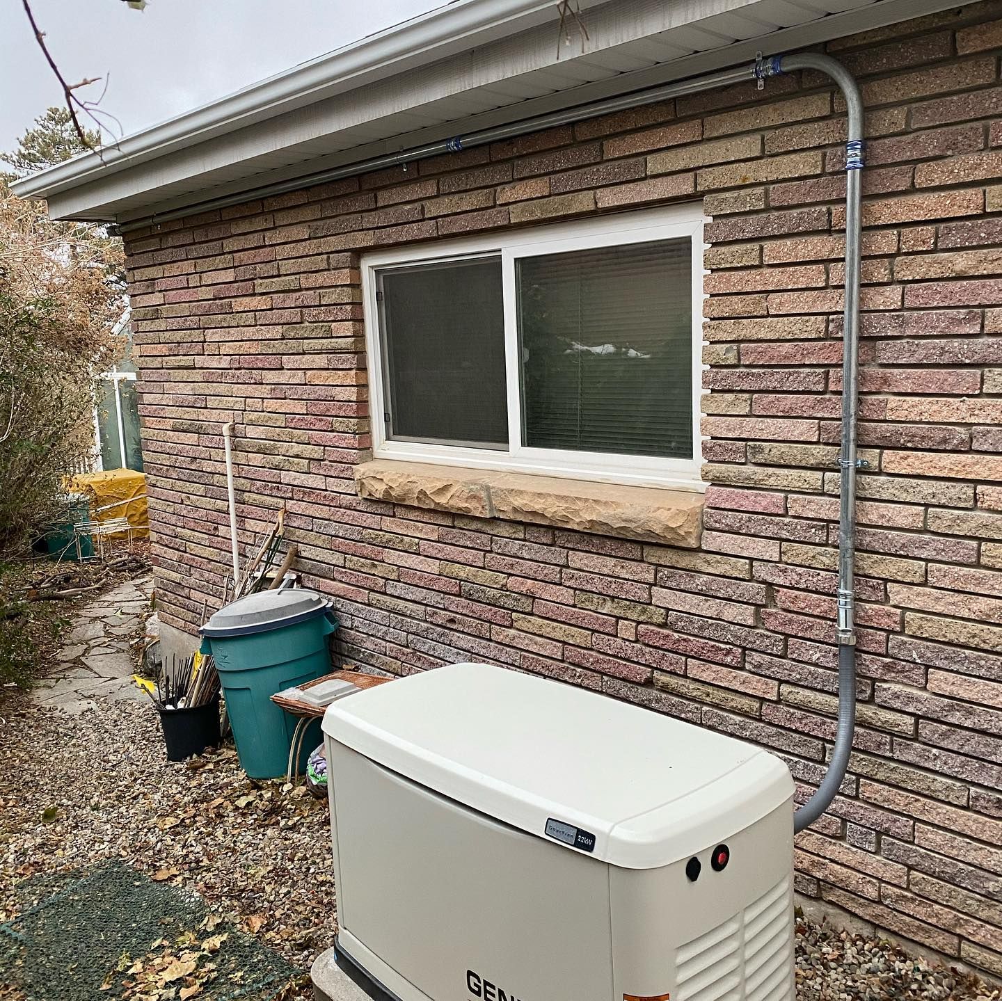 A generator is sitting outside of a brick house next to a window.