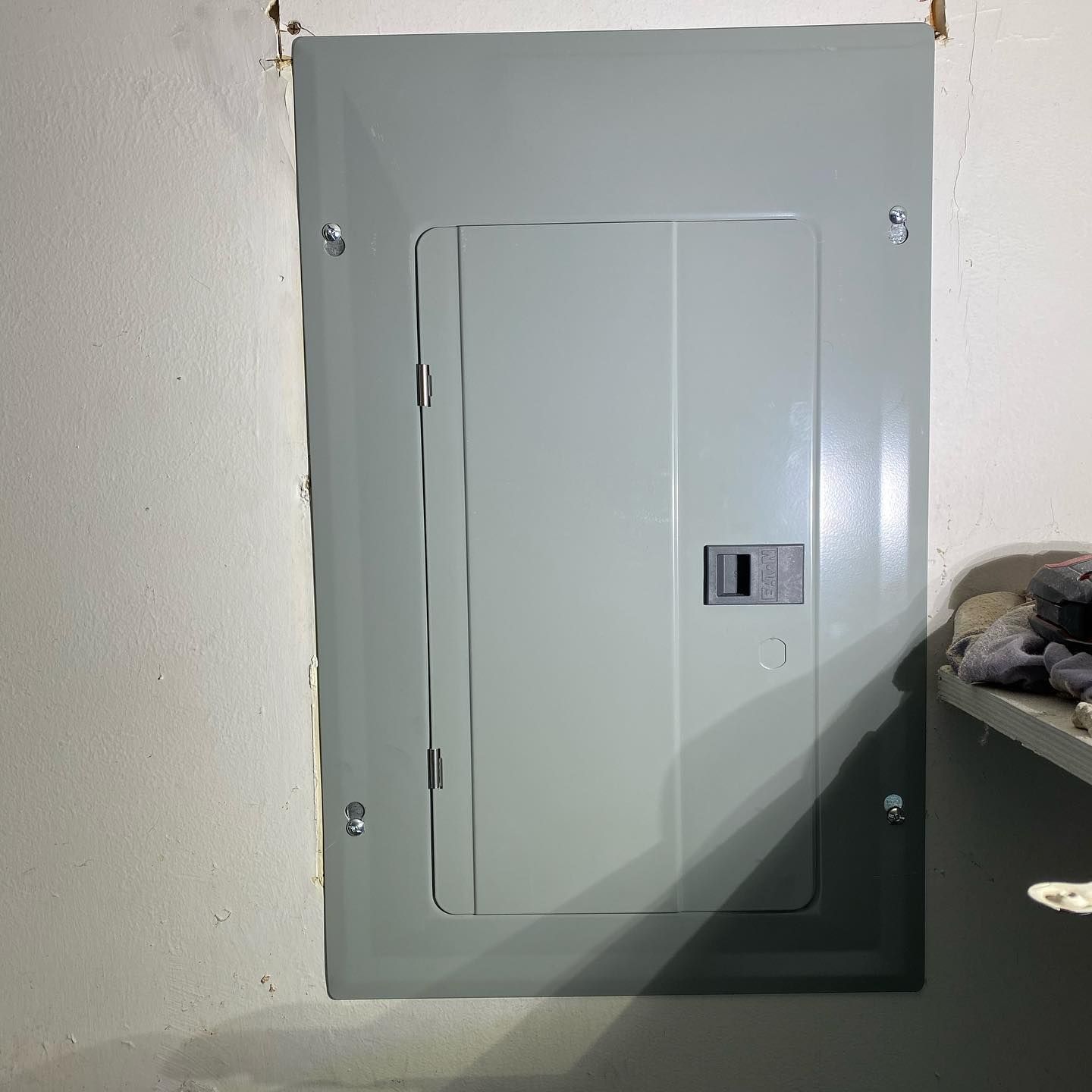 A gray electrical box is sitting on a white wall next to a shelf.
