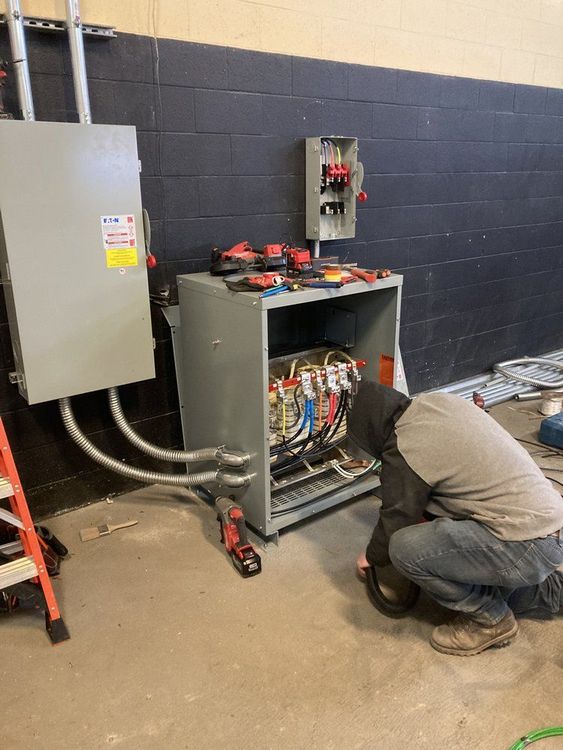 A man is kneeling down in front of a electrical box.