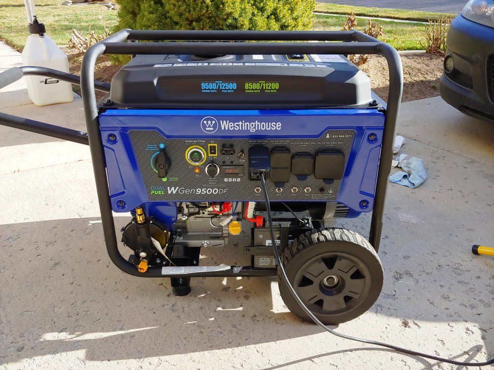 A blue generator is sitting on a concrete driveway next to a car.