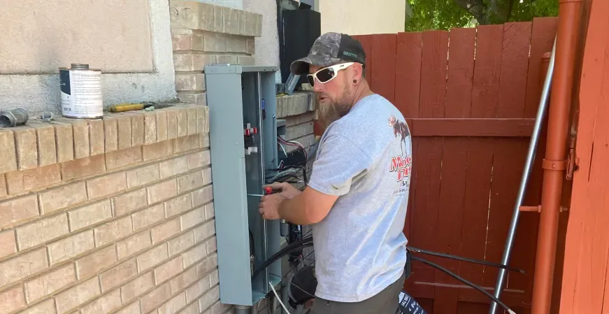 A man is working on an electrical box on a brick wall.