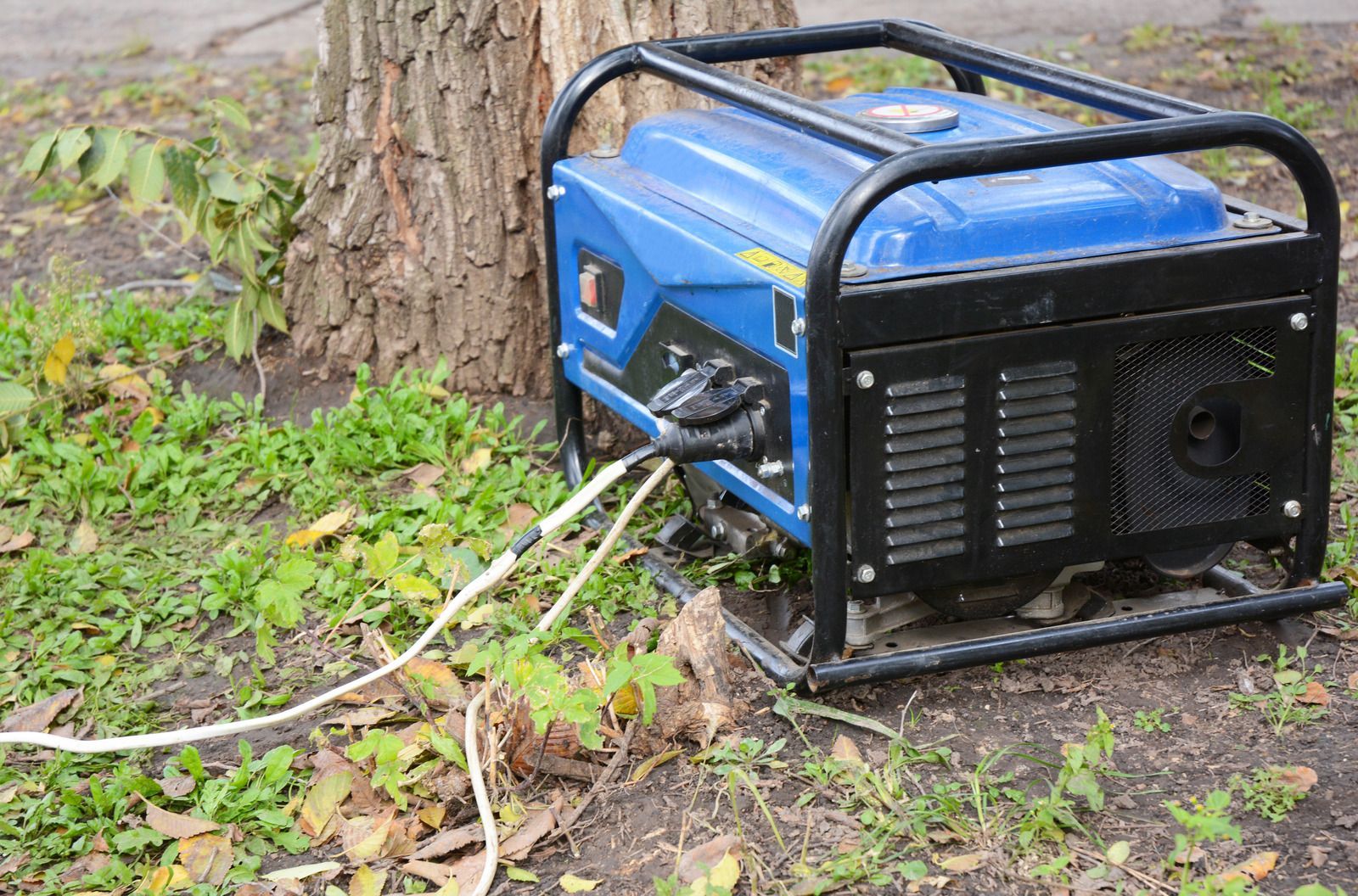 A blue generator is sitting in the grass next to a tree.