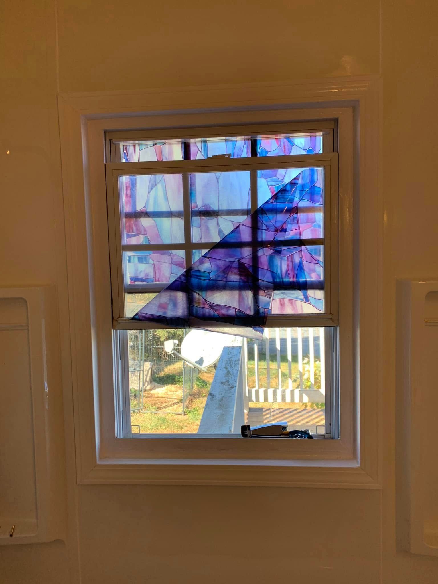 A window with a partial piece of blue, patterned decorative film peeling away from the upper panes.