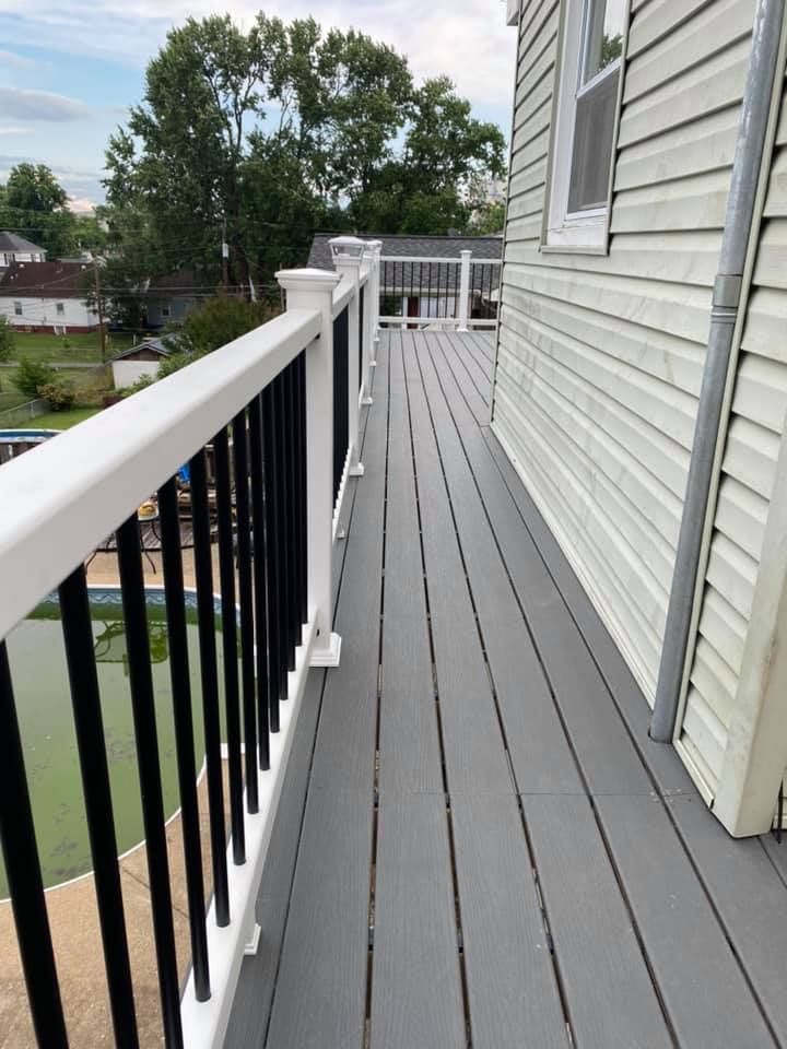 A narrow gray composite deck with white railings and black balusters runs alongside the vinyl-sided wall of a house.