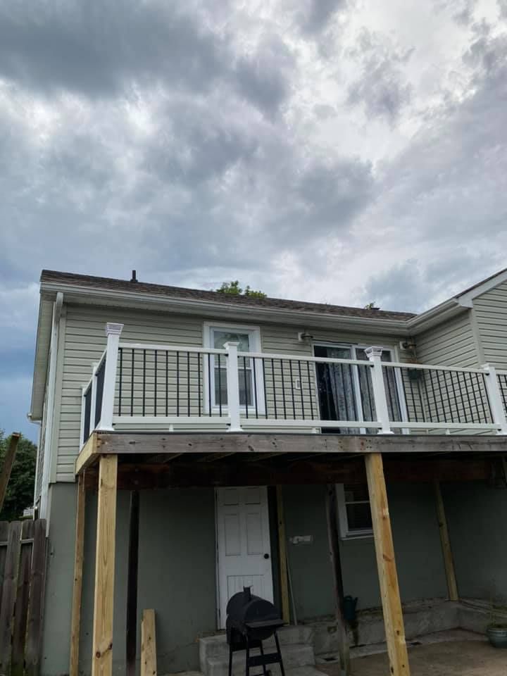 A multi-level house with a second-story deck featuring white railings and black balusters over a gray lower patio area.
