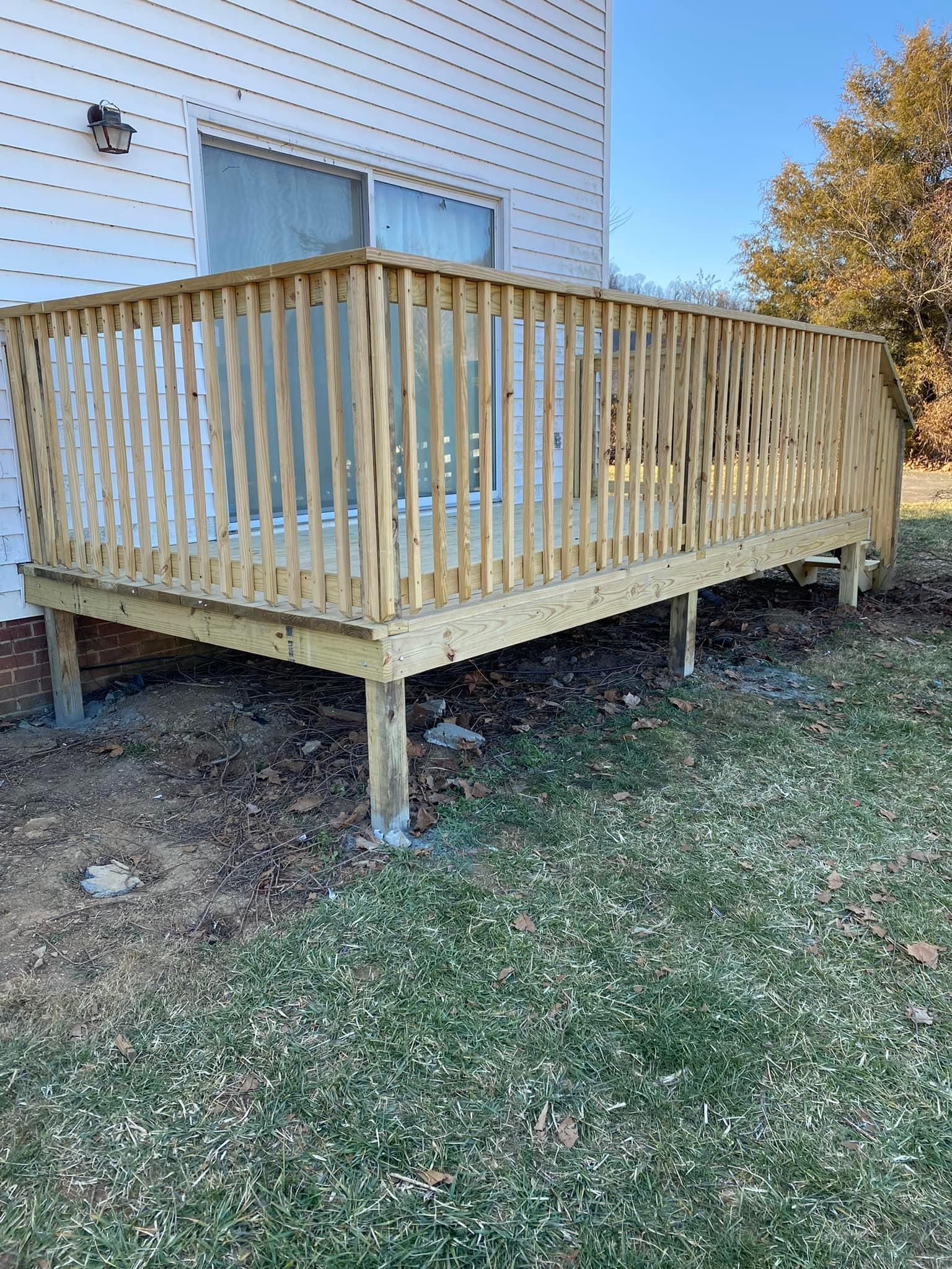 A newly constructed light-wood deck with railings attached to the back of a house, standing on posts over a grassy yard.