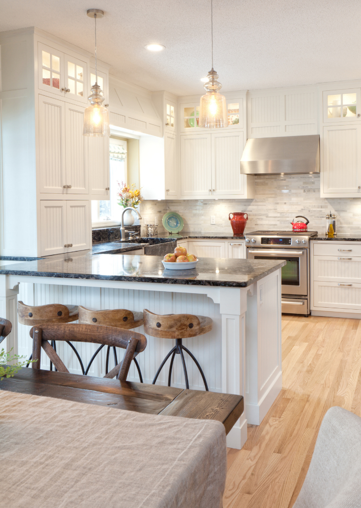 Contact Us Bright kitchen featuring white cabinets, a dark granite island with wooden stools, a stainless steel oven, and wood floors.