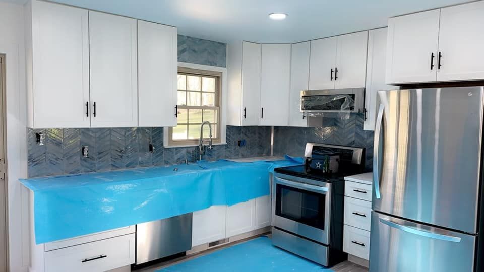 A renovated kitchen featuring white cabinets, stainless steel appliances, and blue protective film covering the counters.