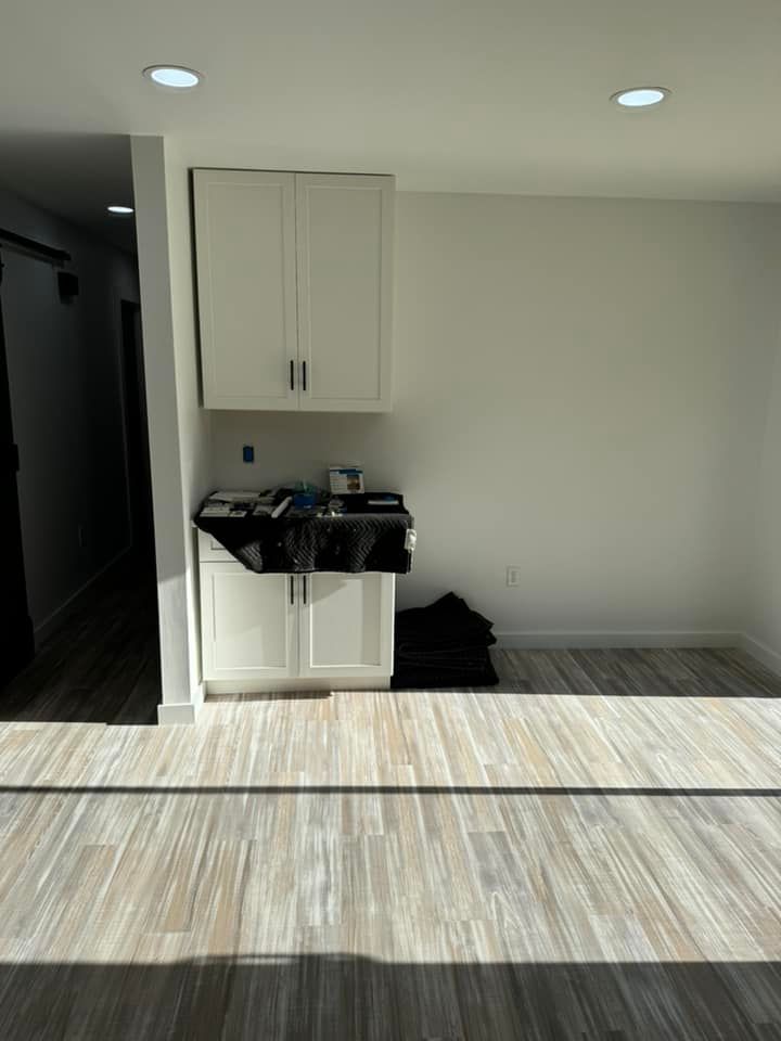 A white kitchen cabinet unit sits against a white wall in a room with light-colored wood-look flooring.