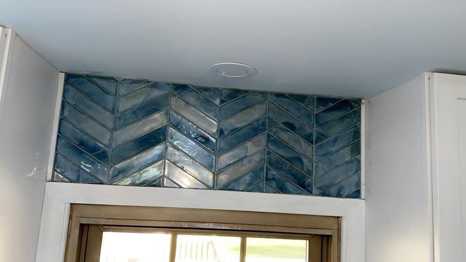 Blue herringbone-patterned glass tiles installed on the wall above a wooden door frame, set against white walls and ceiling.