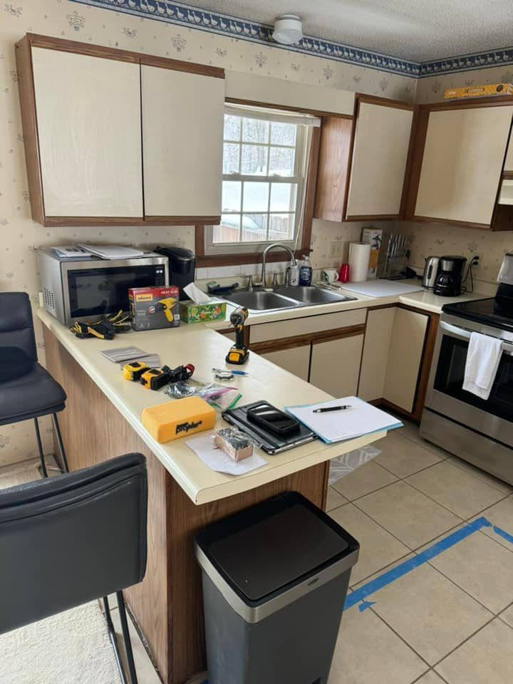 A home kitchen undergoing renovation, featuring tools on a counter, a double sink, wood cabinets, and light tile flooring.