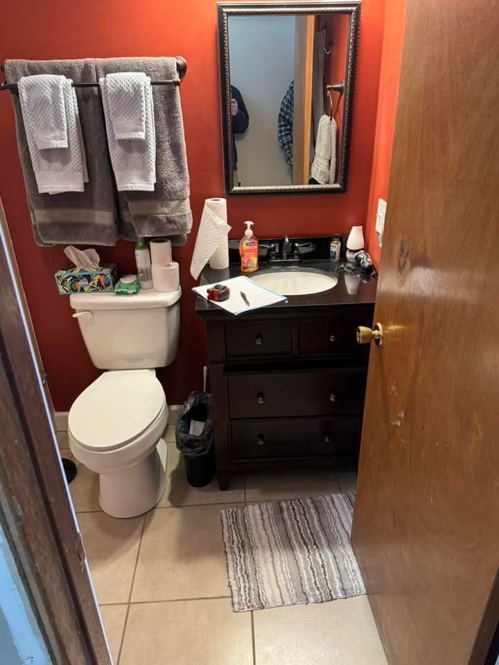 A small bathroom with red walls, a white toilet, dark vanity with a white sink, mirror, and gray towels on a rack.