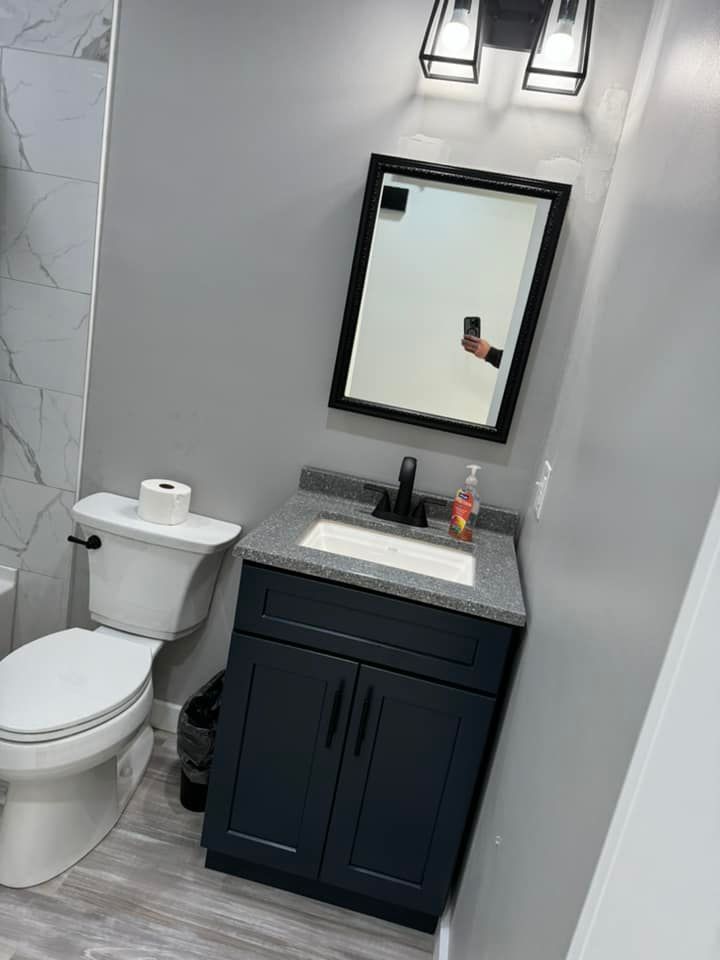 A modern bathroom featuring a navy vanity with a grey countertop, a black-framed mirror, and a white toilet.