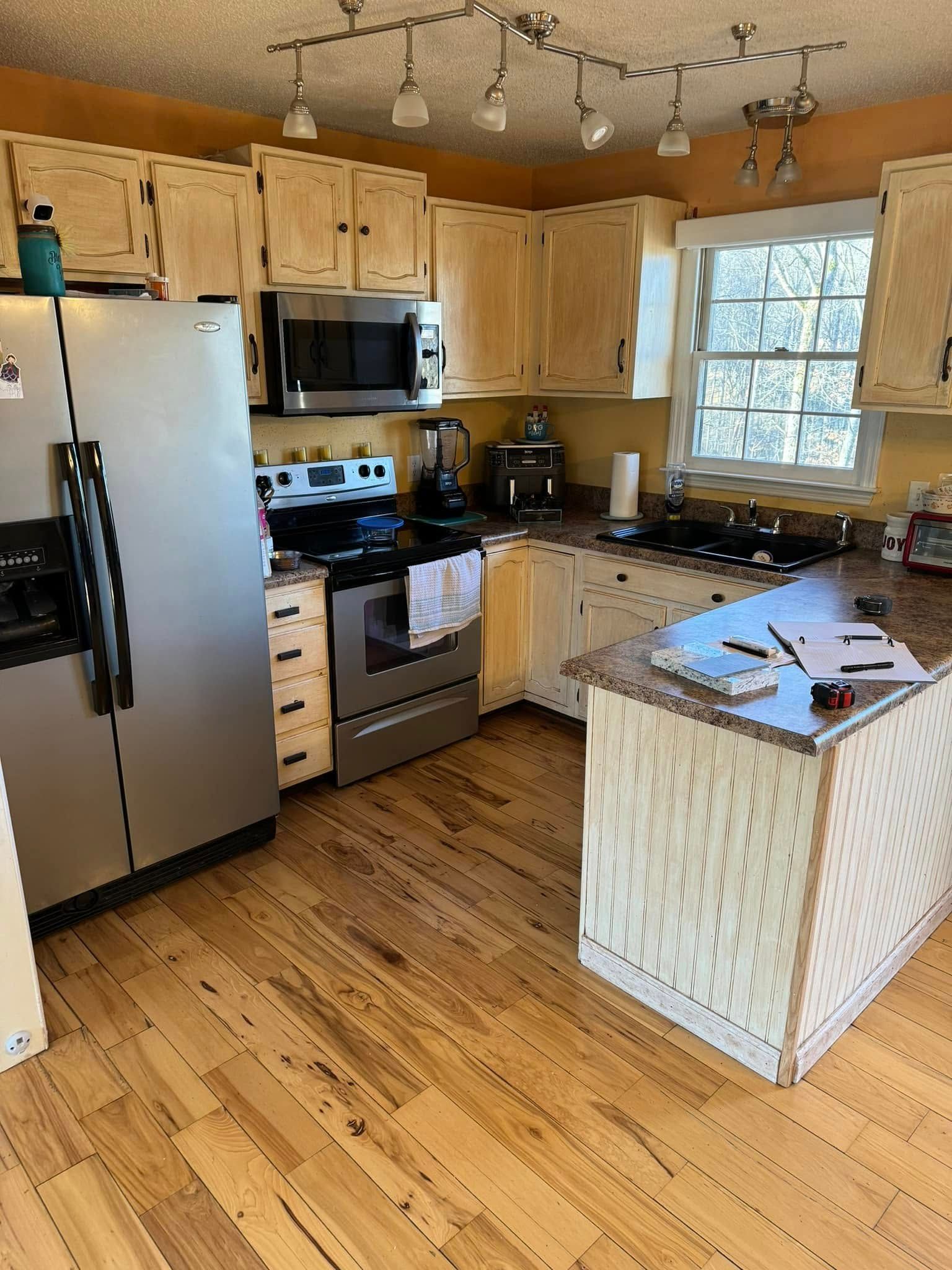 A kitchen with light wood cabinets, stainless steel appliances, a center island, and wood flooring under a track light.