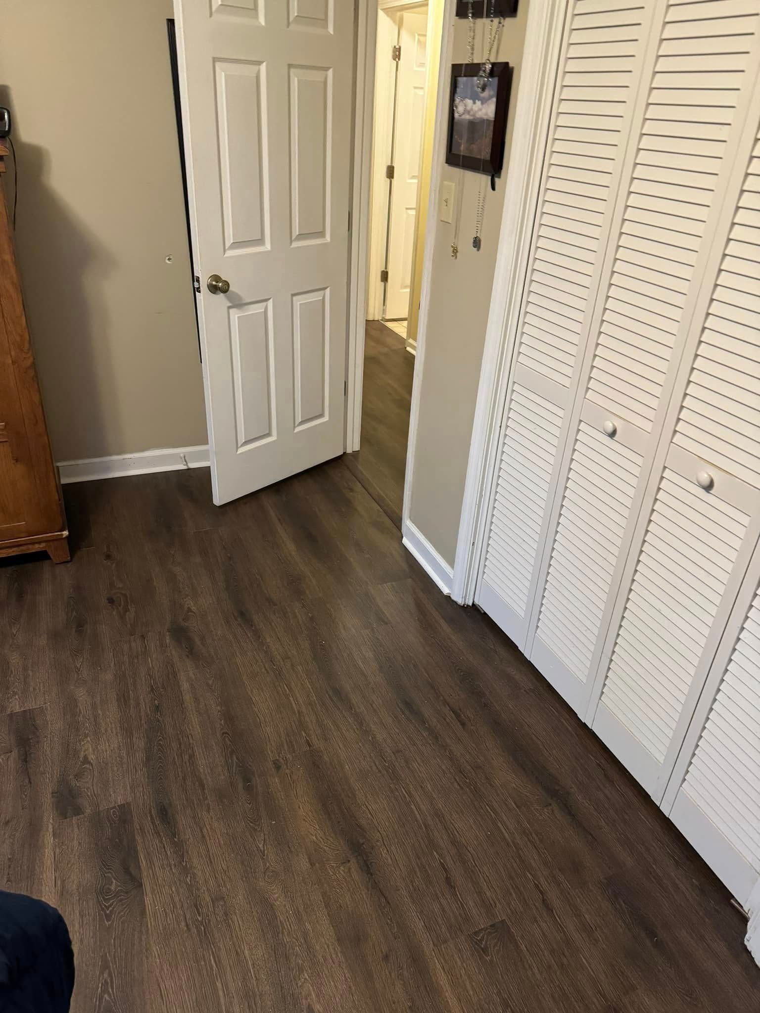 A room with dark wood-look laminate flooring, a white interior door, and a white louvered closet door on the right.