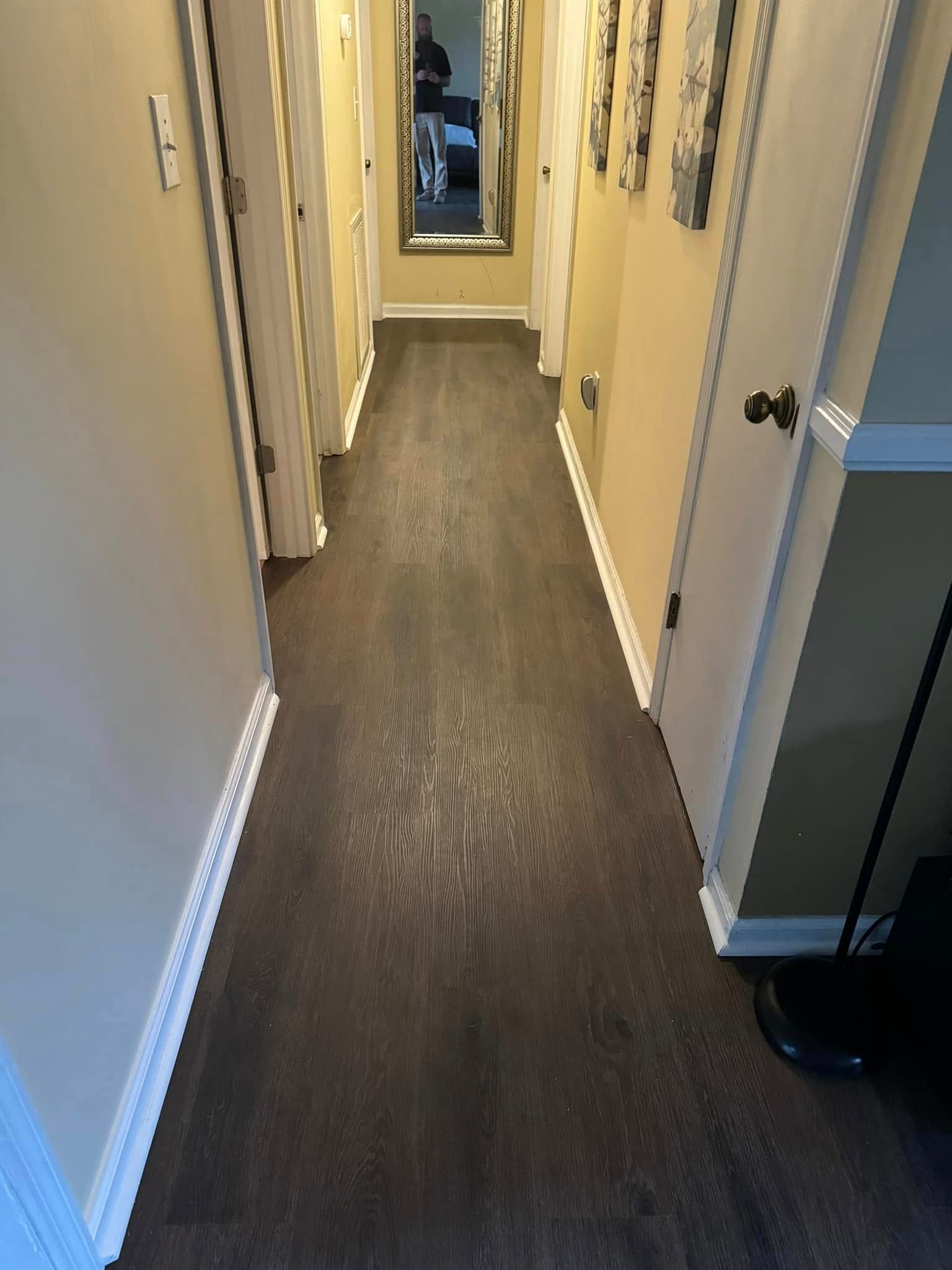 A view looking down a residential hallway with dark wood flooring, beige walls, several closed doors
