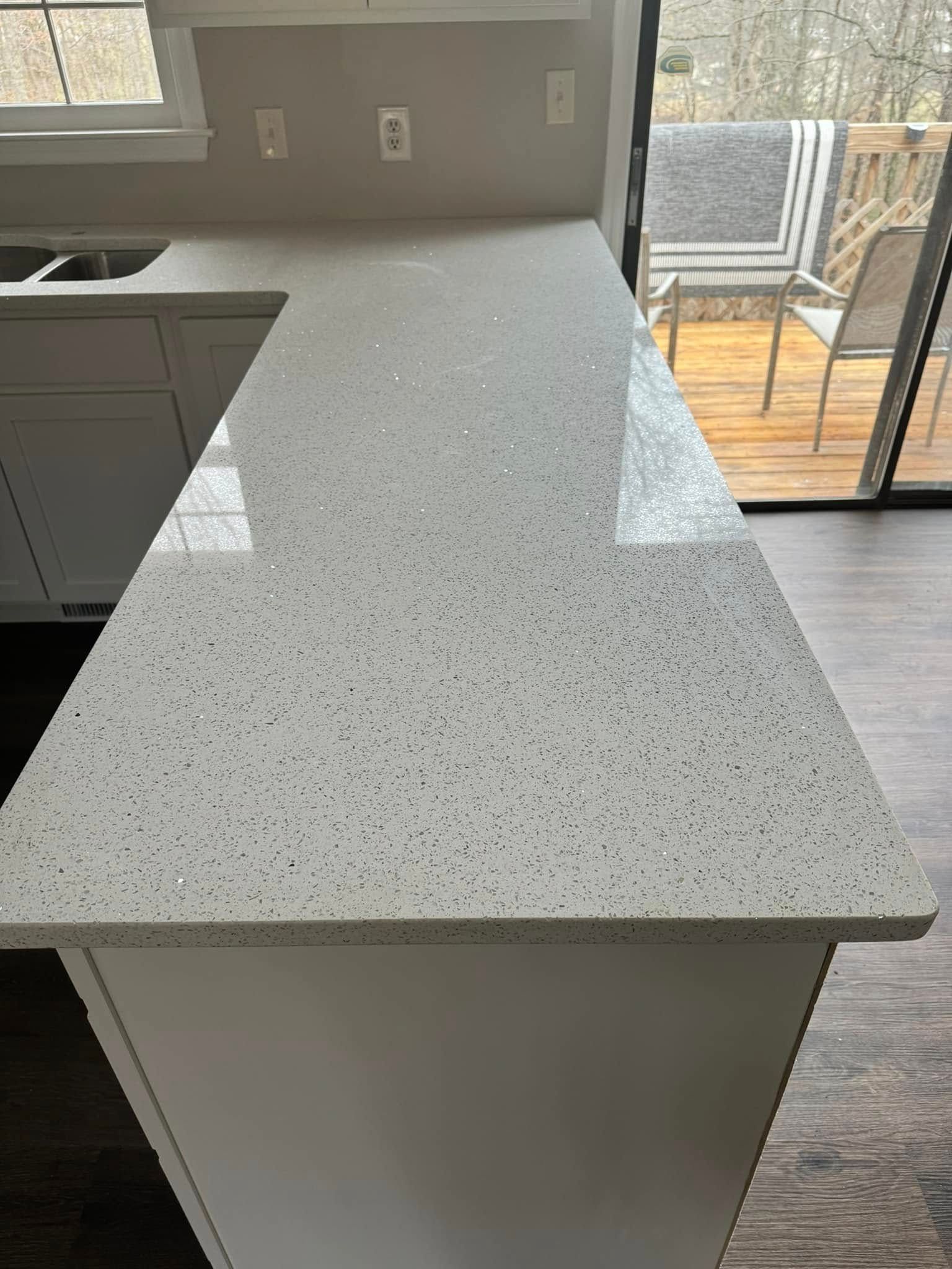A high-angle view of a white, speckled quartz kitchen countertop extending from a sink area toward a sliding glass door.