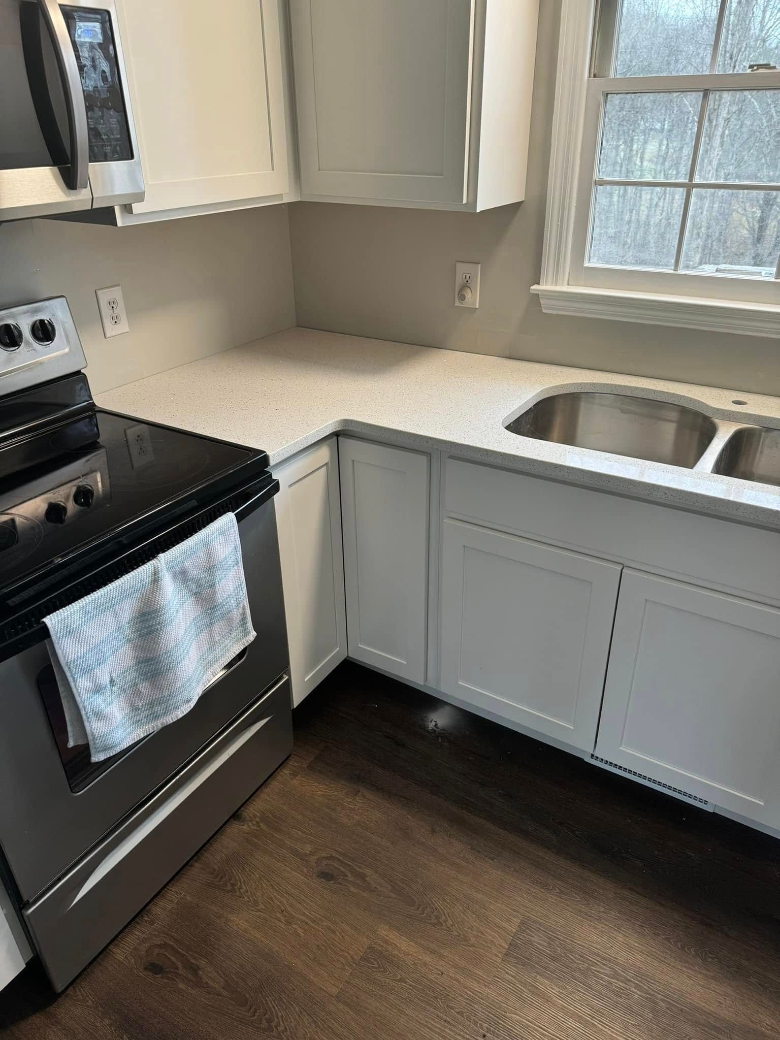 A kitchen corner featuring a stainless steel stove with a patterned towel, white cabinets, and a white-speckled countertop.