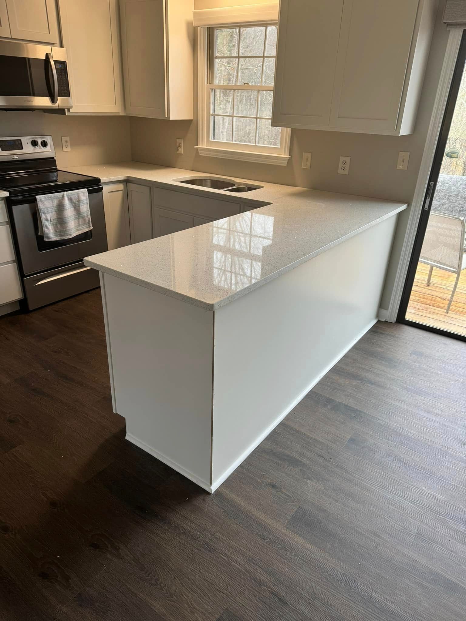 A renovated kitchen featuring white cabinets, light speckled countertops, a gas stove, and dark wood-look floors.