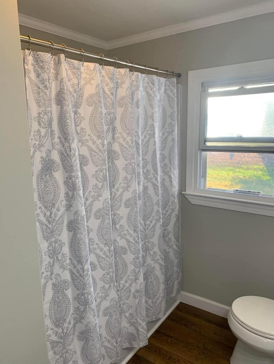 A shower curtain with a white and gray paisley pattern hangs in a bathroom next to a window and a toilet.