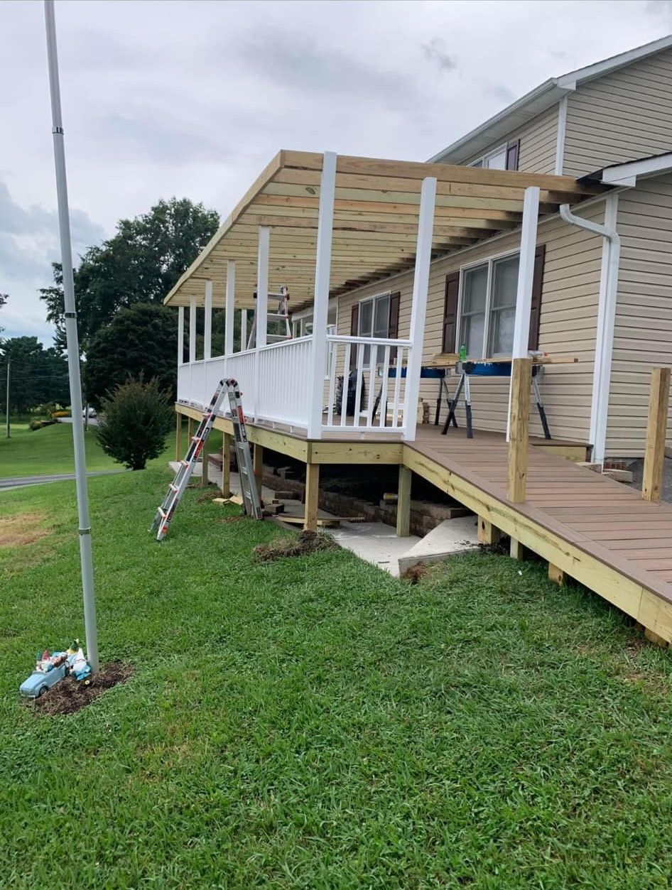 A new wooden deck and porch roof under construction alongside a house, with a wheelchair ramp leading up to it.