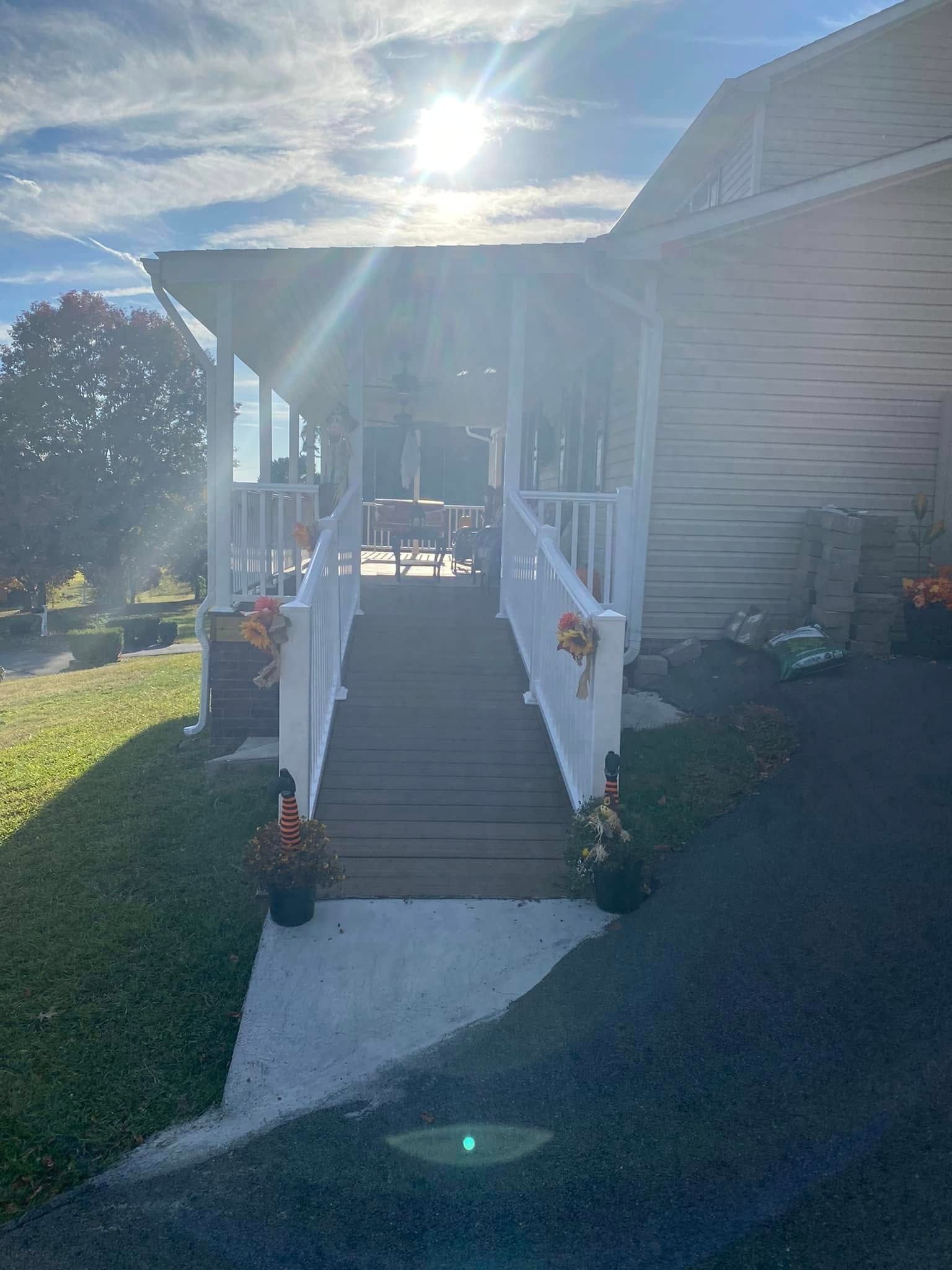 A wooden handicap ramp with white railings leading up to a porch on a sunny day.